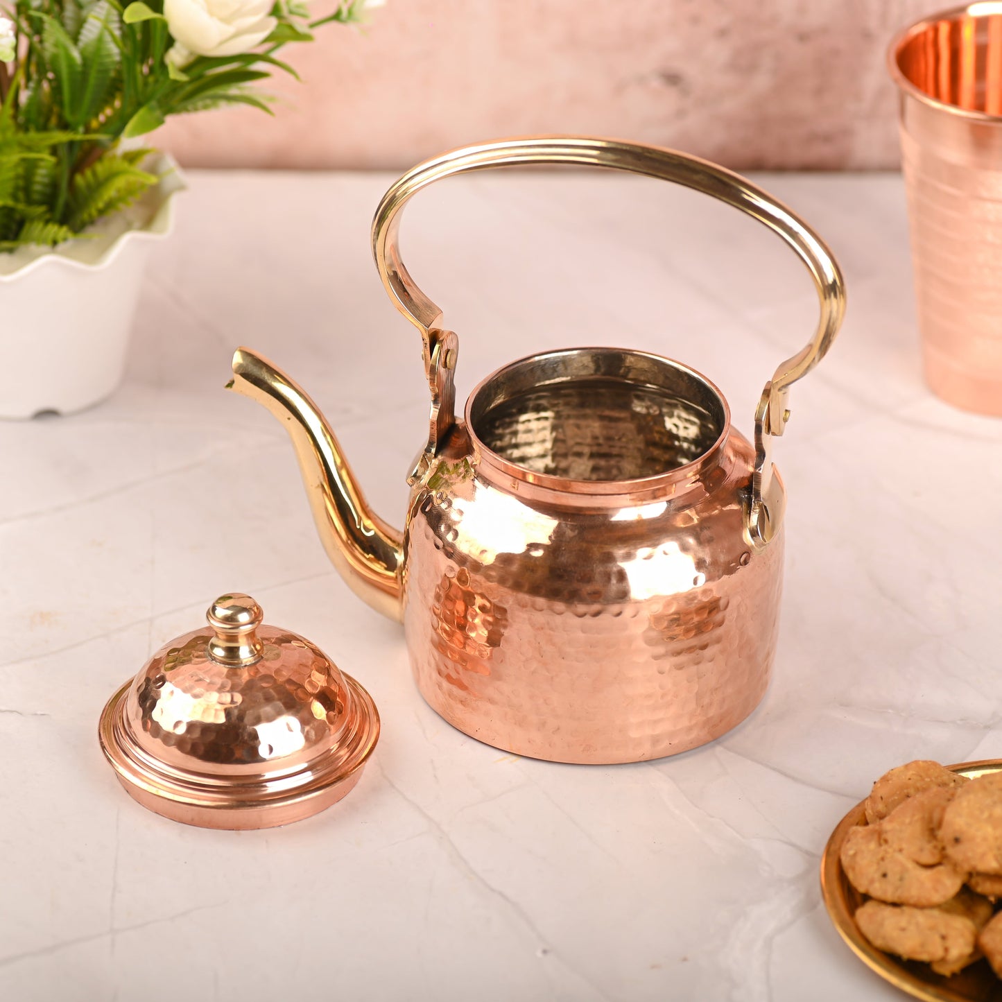 Copper teapot with lid on a light surface with cookies and a cup in the background