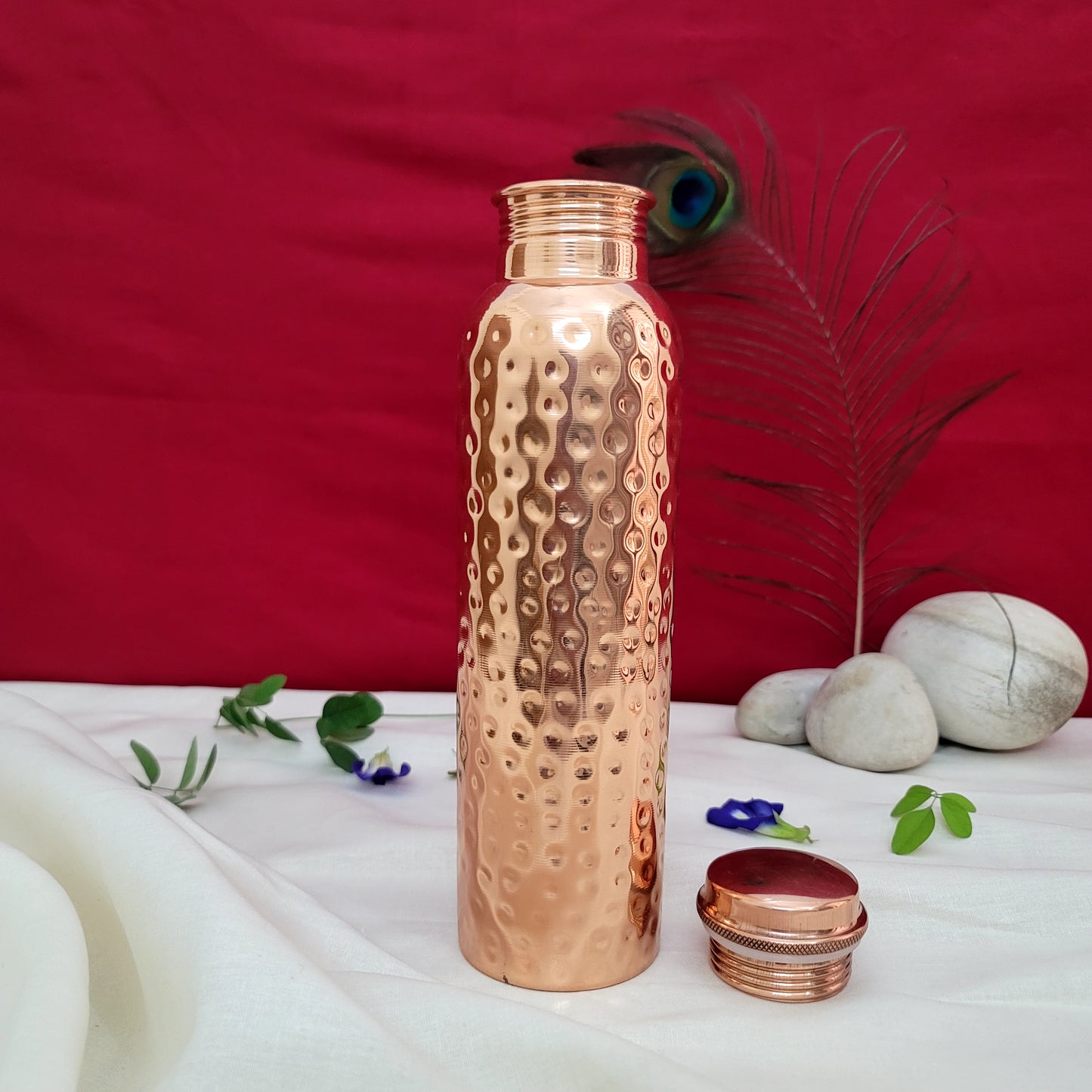 Copper water bottle with a textured design on a white surface with a red background