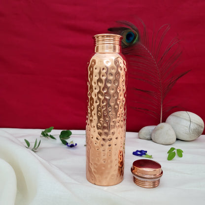 Copper water bottle with a textured design on a white surface with a red background