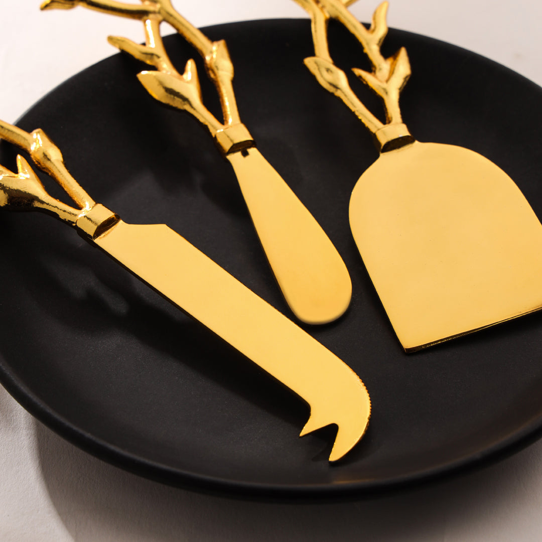 Gold cheese knives and a server on a black plate with a neutral background Sama Homes