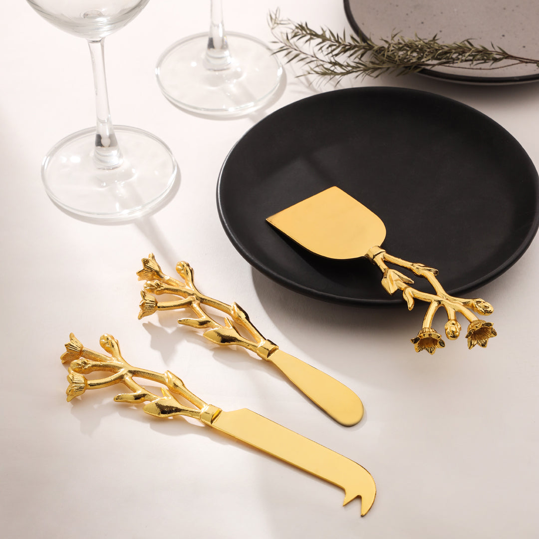 Gold cheese knives with floral design on a black plate with wine glasses and herbs in the background. - Image 3