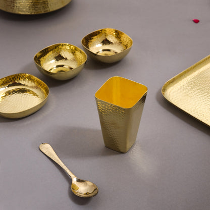 Set of gold metallic bowls, a cup, and a spoon on a gray surface