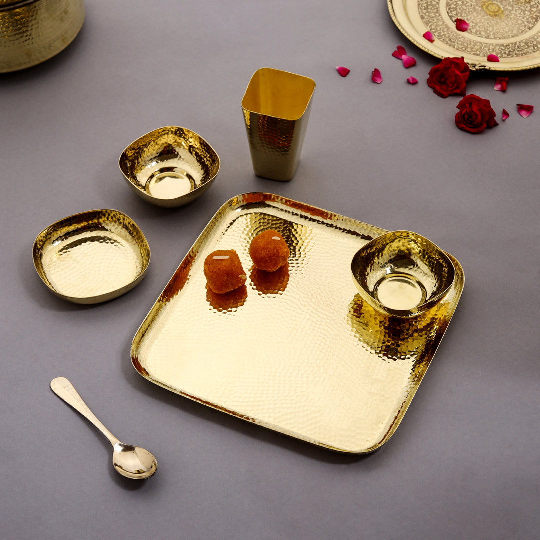 Gold metallic tray with smaller dishes, cup, and spoon on a gray background with decorative elements.