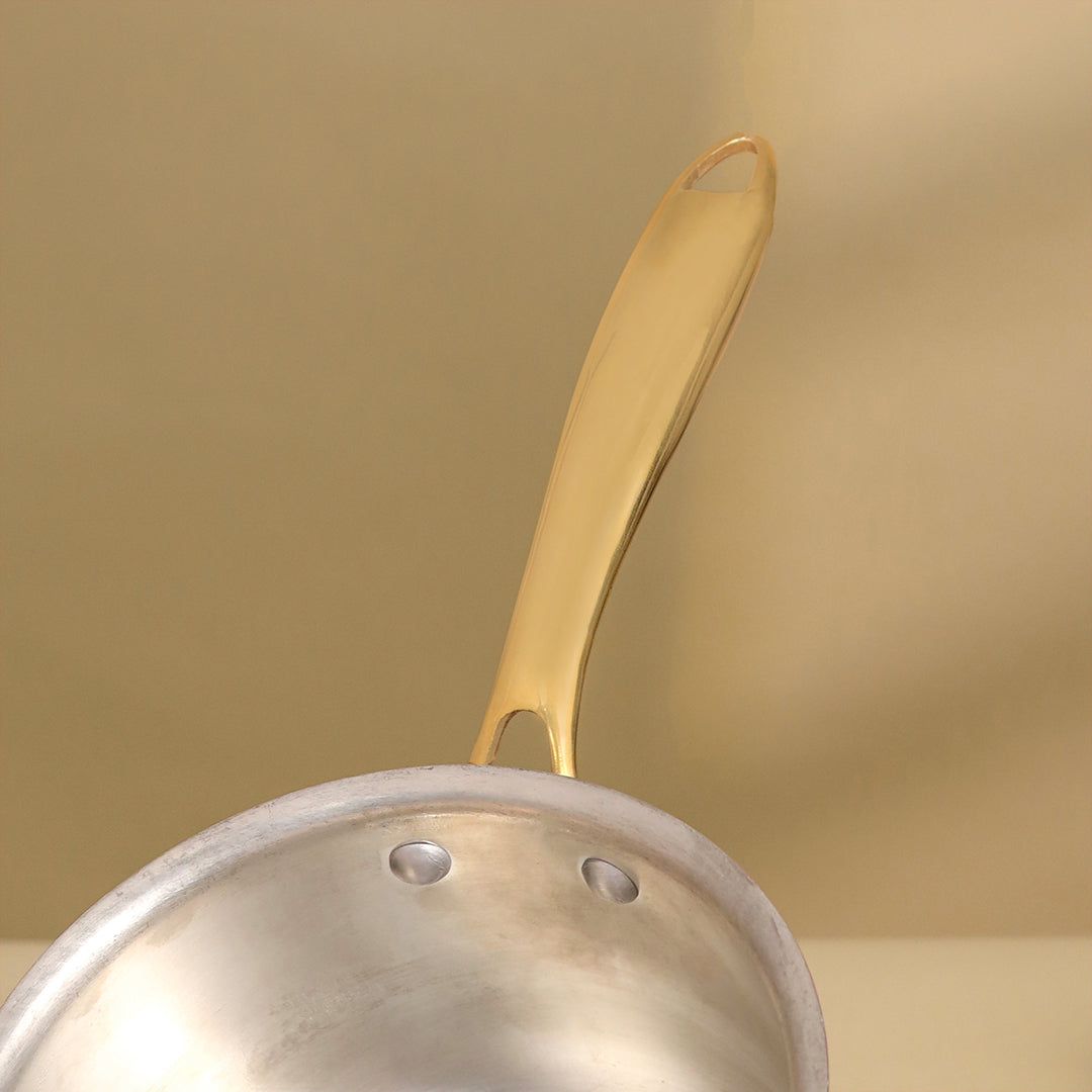 Close-up of a silver pot with a gold handle on a beige background