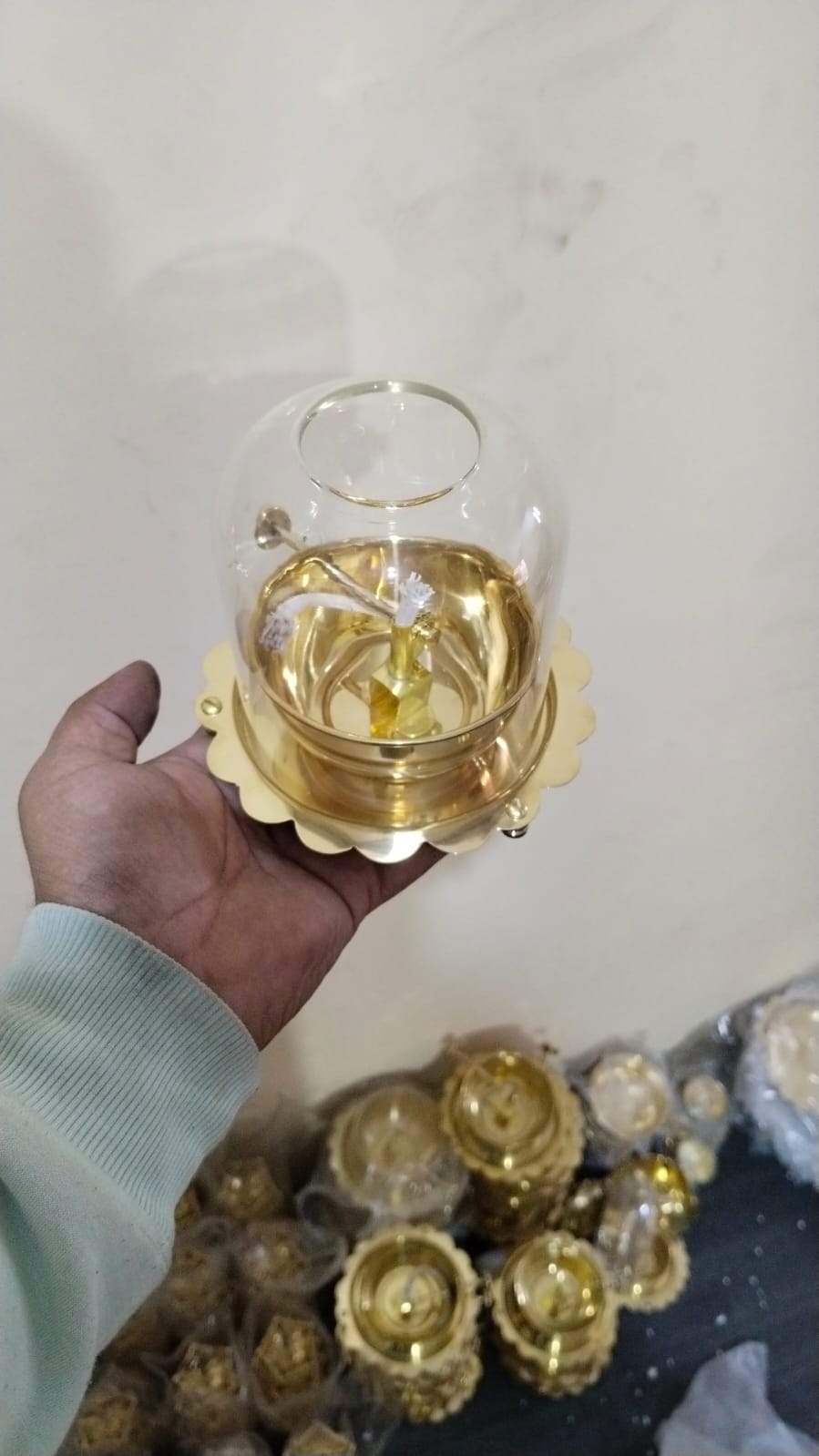 Hand holding a small glass container with a gold base on a light background - Image 2