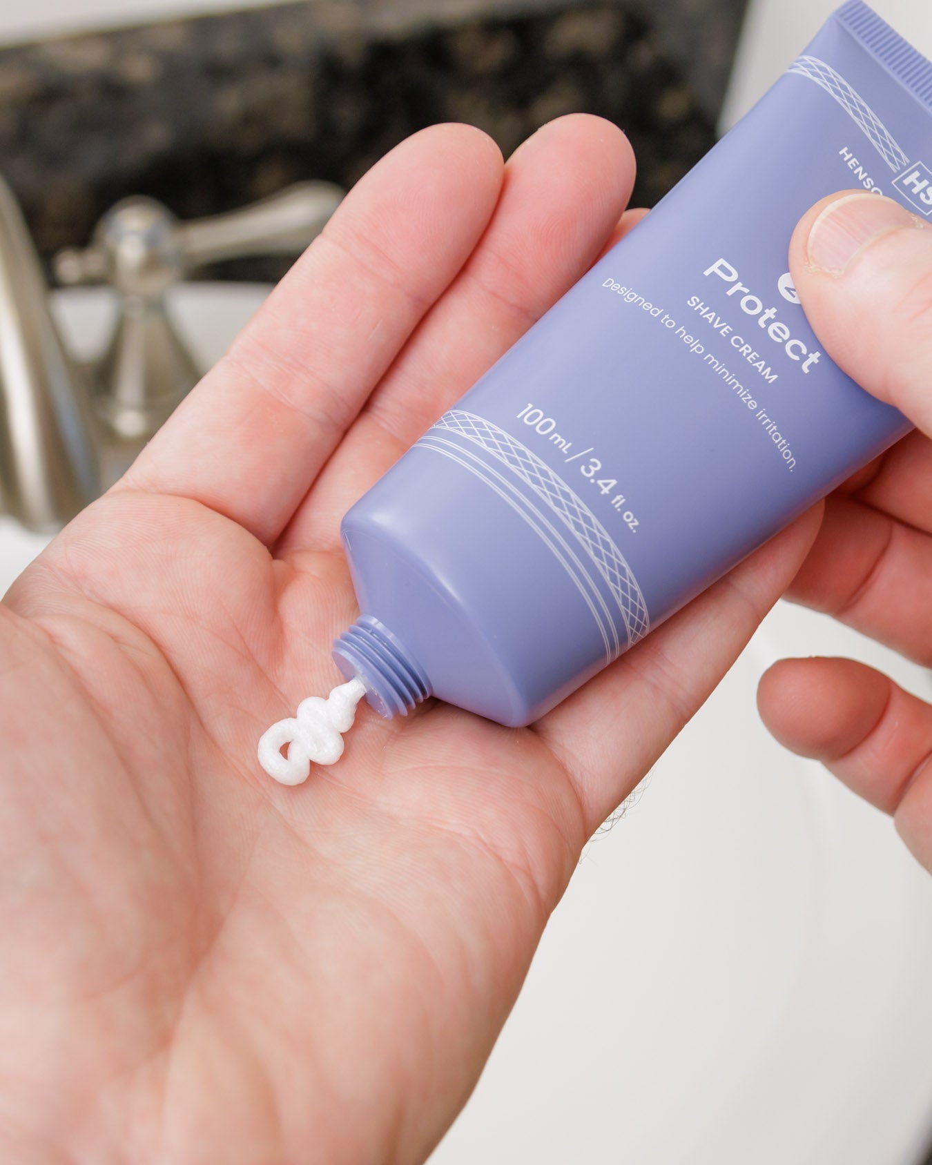 Hand holding a purple bottle of sunscreen cream with a small amount on the palm.